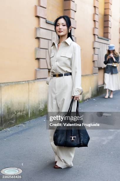 Guest wears silver earrings, a black leather Tod's bag, a black leather bag, brown leather shoes and a beige cargo long-sleeved jumpsuit outside...