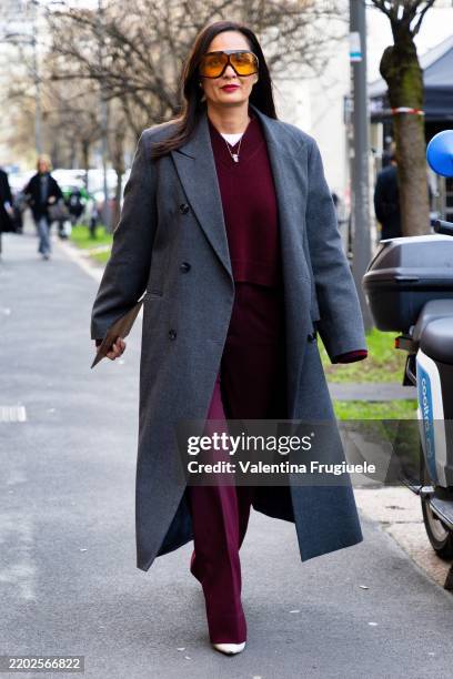 Guest wears black sunglasses, a burgundy sweater, a white t-shirt, a grey coat, white pumps and burgundy flared trousers outside Tod's during the...