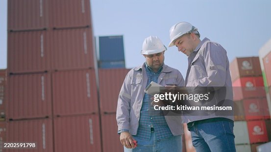 Manager talking with engineer or supervisor about loading container from cargo freight ship for transportation in loading zone at cargo terminal. Professional business team working together in logistic business. Concept of logistics business, transport. Manager talking with engineer or supervisor about loading container from cargo freight ship for transportation in loading zone at cargo terminal. Professional business team working together in logistic business. Concept of logistics business, transport.
