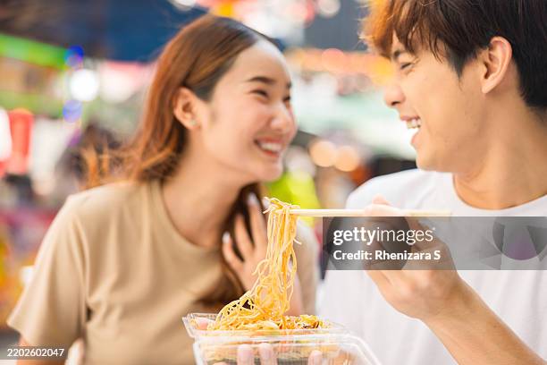 young asian couple savoring authentic thai street food at a bustling bangkok night market, capturing the vibrant essence of local cuisine and culture during their culinary adventure. - thai food stock pictures, royalty-free photos & images