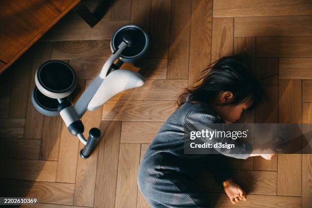 asian toddler girl throwing a tantrum lying on the wooden floor next to her tricycle at home. seeking for attention and company. children's growth and development. kids emotions and feelings - stubborn stock pictures, royalty-free photos & images