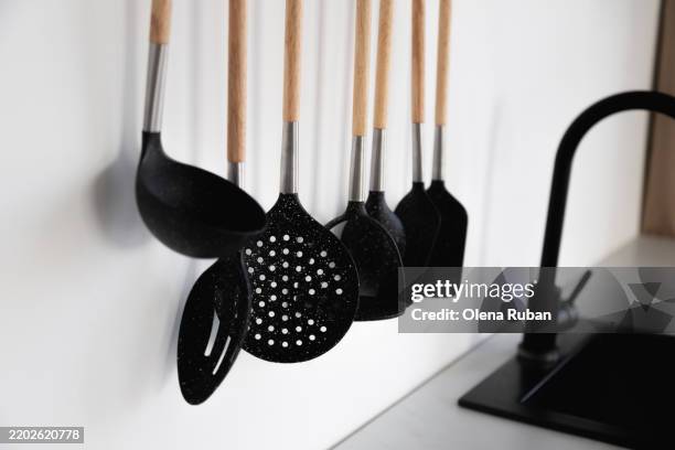 kitchen utensils hanging near a black sink with a water tap. - spatula stock pictures, royalty-free photos & images
