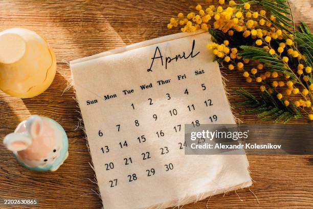 april 2025 calendar, mimosa branches flowers and easter decoration on wooden table background. flat lay. hello spring concept - avril photos et images de collection