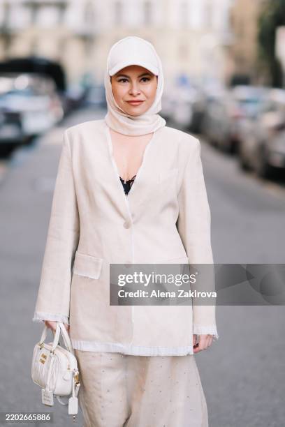 Guest is seen wearing a cream oversized blazer, trousers, a headscarf and cap, white sneakers, a white handbag outside the Sportmax show during the...