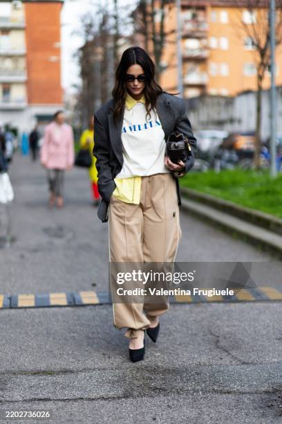 Vivian Bénard wears black platform heels, black sunglasses, a grey striped blazer, a yellow shirt, a white printed t-shirt, a bordeaux leather bag...