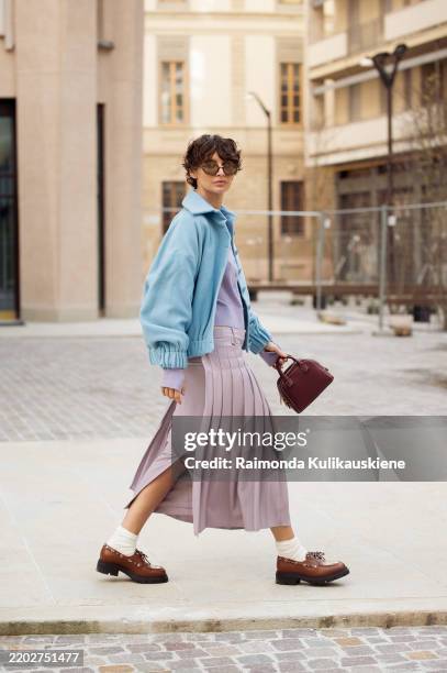 Irina Kro Eicke wears lavender midi skirt with attachable pleated part, matching top with buttons, white socks, brown loafers, blue jacket and brown...