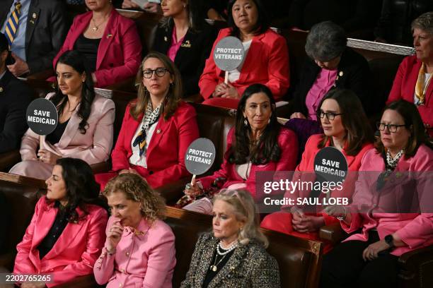 Democratic members of Congress hold up signs reading "Save Medicaid" and "Protect Veterans" as US President Donald Trump speaks during an address to...