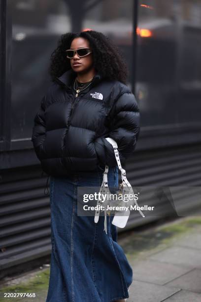 Fashion Week Guest seen wearing a black puffer The North Face jacket, denim jeans skirt, white Le Cagole Balenciaga handbag with charms outside SRVC...