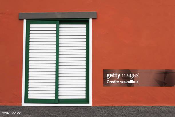 Closed window shutters. White paint window shutters background. Architecture texture. Object isolated on red house wall facade.