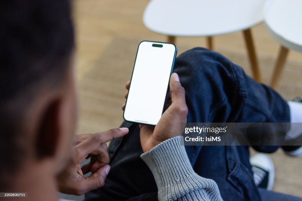 Young man relaxing on sofa using smartphone with blank screen