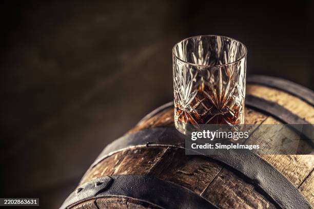 glass of whisky cognac rum or bourbon in ornamental glass on old wooden barrel - keg stock pictures, royalty-free photos & images