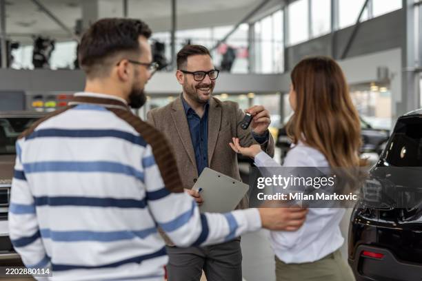 happy car salesman giving keys to a couple in a dealership - autokredit stock-fotos und bilder