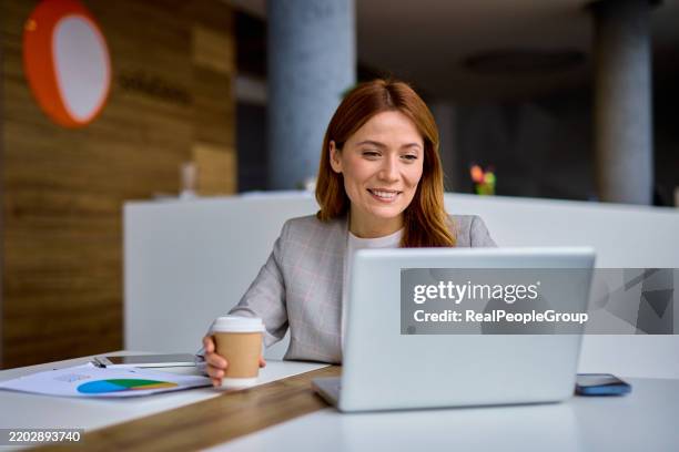 businesswoman smiling and working with laptop in modern office - female likeness stock pictures, royalty-free photos & images