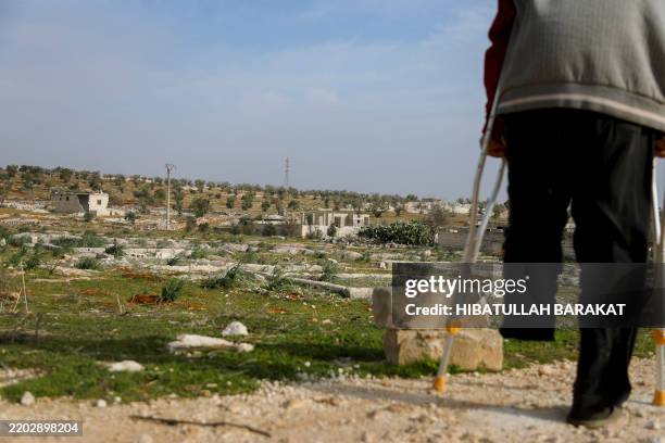 Nidal Ahmad walks with crutches towards his farmland in Aleppo, Syria, on March 4, 2025. The proximity of his olive farm to a military camp known as...