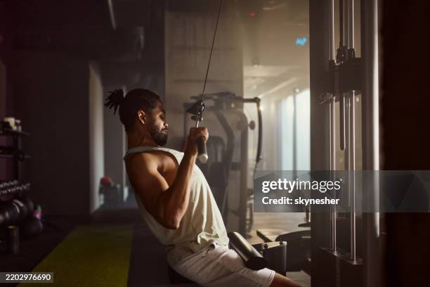 black sportsman exercising on lat pull down machine in a gym. - pulling stock pictures, royalty-free photos & images
