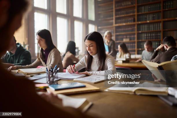 joven estudiante leyendo un libro de texto en la biblioteca. - estudiante de universidad fotografías e imágenes de stock