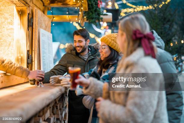 friends enjoying mulled wine at holiday market counter with festive lights - julmarknad bildbanksfoton och bilder