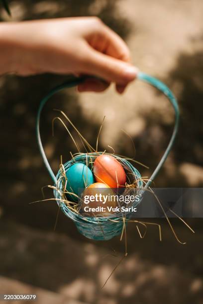 hand holding a basket of colorful eggs - easter egg hunt stock pictures, royalty-free photos & images