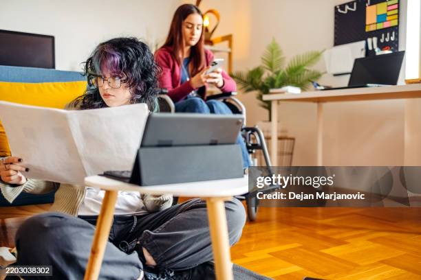 young female adult in wheelchair study together with roommate at apartment who is sitting on floor while looking at paper document - disability computer stock pictures, royalty-free photos & images