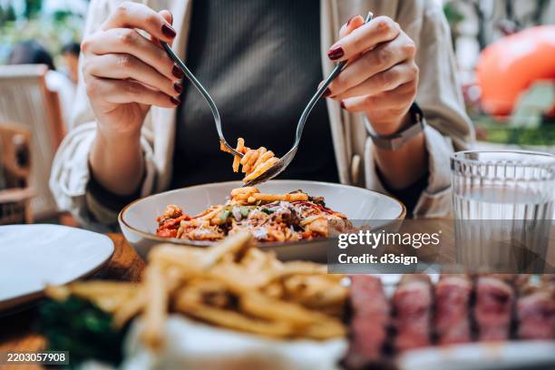 close-up, mid-section of young asian woman sitting at dining table holding cutleries, twirling freshly served spaghetti bolognese and enjoying her meal in restaurant. dining out. people, food and lifestyle - tradizione foto e immagini stock