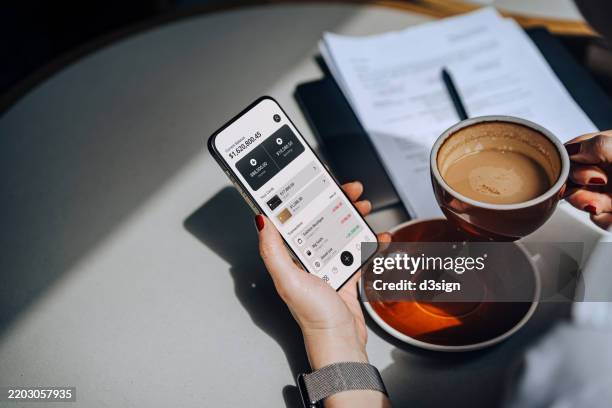 cropped shot of a woman accessing online banking with mobile app on smartphone to manage her banking needs in a cafe. managing finance and investment at easy access. wealth management. smart banking with technology - investering stockfoto's en -beelden