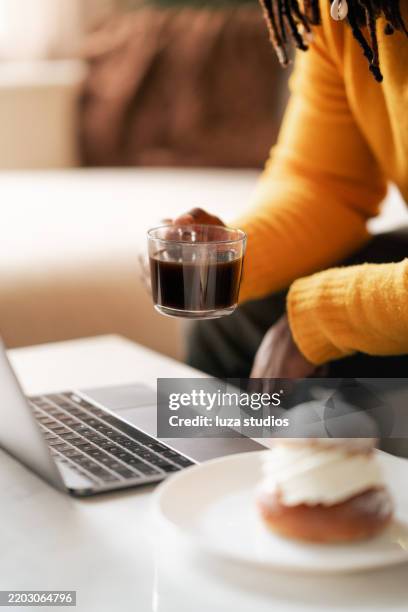man enjoying coffee and pastry while working on laptop at home - grädde bildbanksfoton och bilder