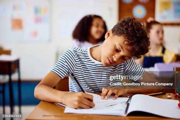 elementary schoolboy concentrating at desk, writing notes in notebook - elementary age stock pictures, royalty-free photos & images