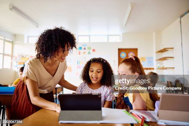 happy young female teacher explaining to schoolgirls using digital tablet, laughing - criança de escola primária imagens e fotografias de stock