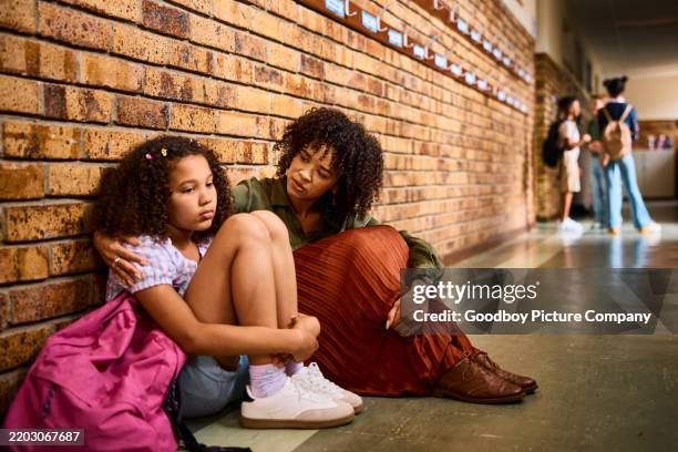 elementary school teacher consoling schoolgirl leaning on wall looking sad in school corridor - consoling stock pictures, royalty-free photos & images
