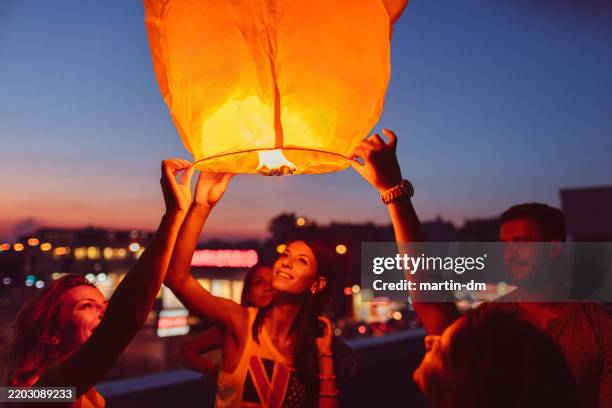 friends on rooftop party releasing paper lantern - releasing lanterns stock pictures, royalty-free photos & images