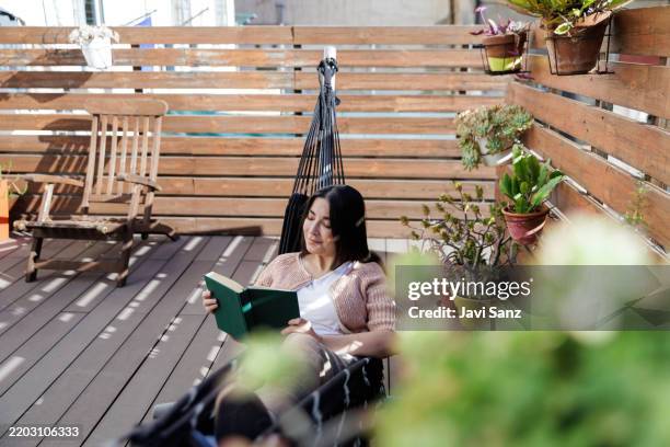 woman relaxing on terrace hammock reading book - terras stockfoto's en -beelden