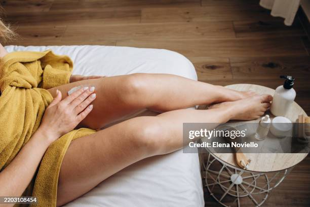 woman appling moisturizing lotion to her thigh skin, body cream after showering - creme corporal imagens e fotografias de stock