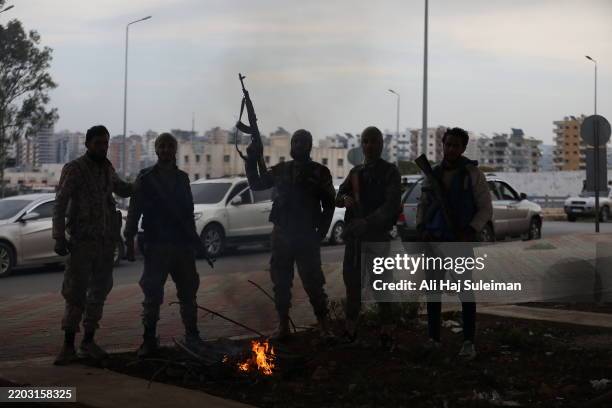 Fighters with the new Syrian government stand around a fire on March 7, 2025 in the Tartus region of Syria. Dozens of people have been killed in...