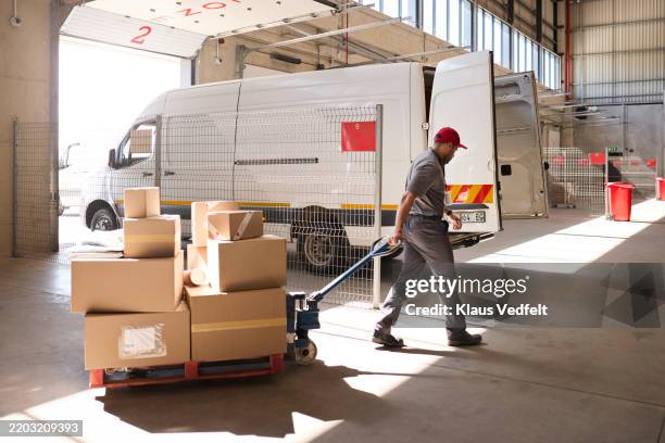 delivery man pulling hand truck of cardboard boxes - veicolo terrestre commerciale foto e immagini stock