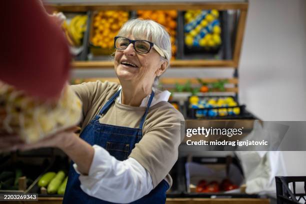 supermarket employee assisting female customer with fresh fruit purchase - werkende bejaarden stockfoto's en -beelden
