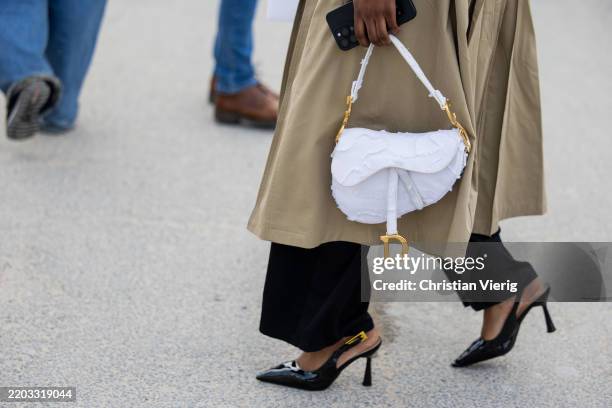 Guest wears white saddle bag, heels, trench coat, black pants outside Dior during the Womenswear Fall/Winter 2025/2026 as part of Paris Fashion Week...