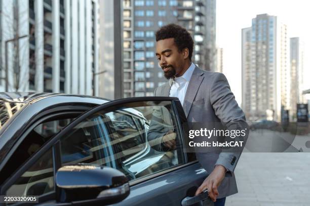mann öffnet fahrzeugtür in moderner urbaner umgebung tagsüber - limousine familienfahrzeug stock-fotos und bilder