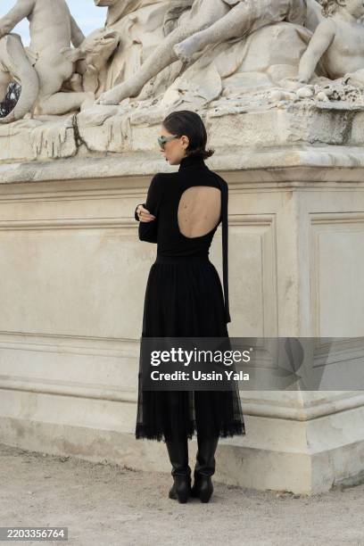 Adele Khalilzade is wearing a black leather jacket, a black dress, black boots, green sunglasses, a red bag and a black scarf outside Dior during the...