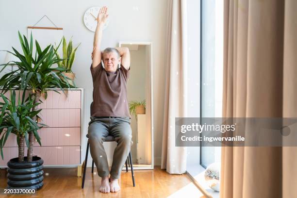 cheerful senior man with grey hair and is stretching at home - home workout stock pictures, royalty-free photos & images