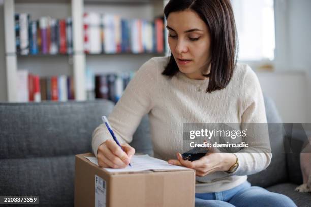 female customer filling out a return request for a delivered package - reembolso imagens e fotografias de stock