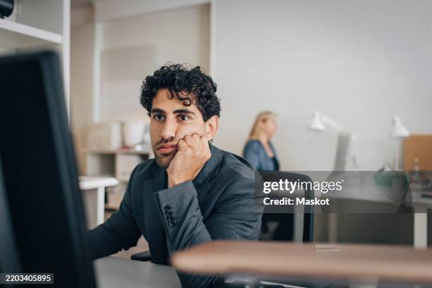 tired businessman leaning on elbows while using desktop pc in office - exclusion photos et images de collection