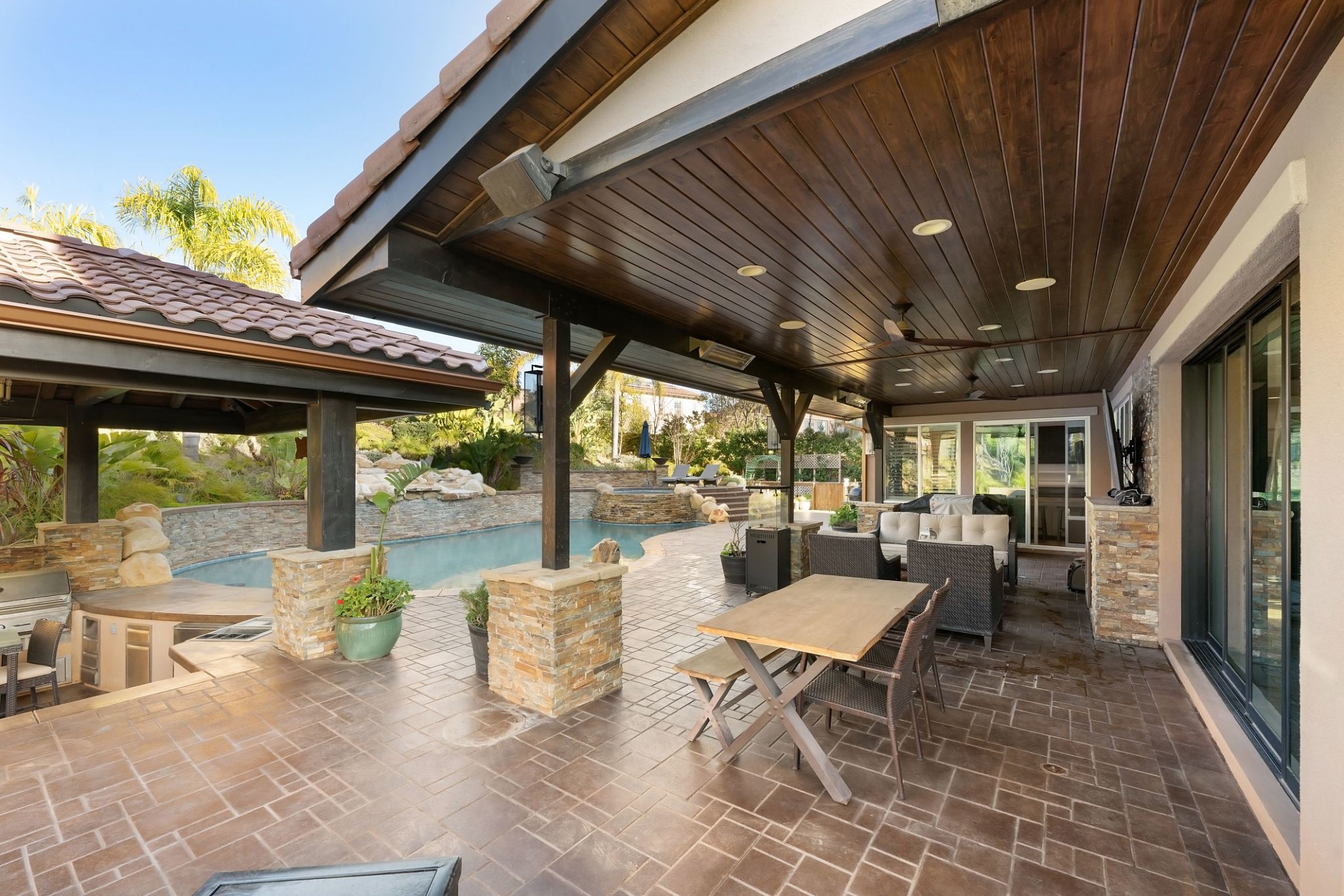 Luxury outdoor living space with covered patio, pool, lush landscaping, and stone accents Luxury outdoor living space with covered patio, pool, lush landscaping, and stone accents