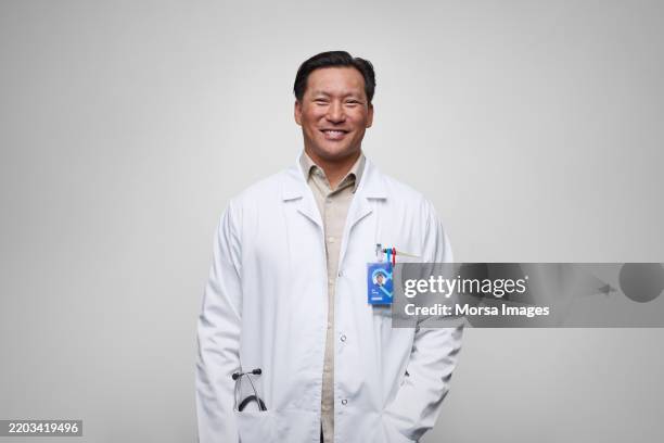 confident asian doctor against white background - bata de laboratorio fotografías e imágenes de stock