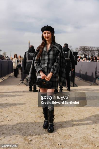 Guest wears black beret, dark gray plaid pattern tailored buttoned up Dior blazer jacket, dark gray plaid pattern Dior scarf, dark gray plaid pattern...