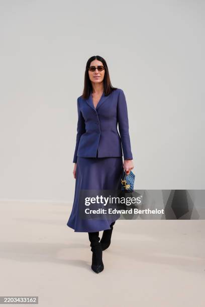 Guest wears black sunglasses, dark navy blue tailored Dior blazer jacket, navy blue Dior midi skirt, black pointed toe slouchy heels suede shoes,...