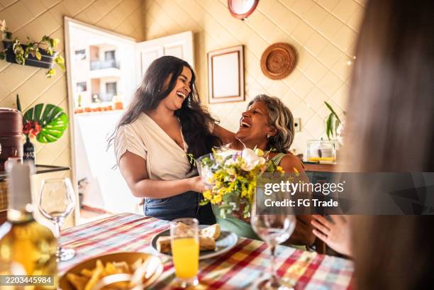 mujer joven dando flores a su madre en casa - día de la madre fotografías e imágenes de stock