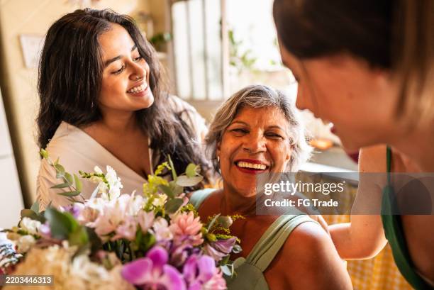 young sisters giving flowers to mother at home - familie met meerdere generaties stockfoto's en -beelden