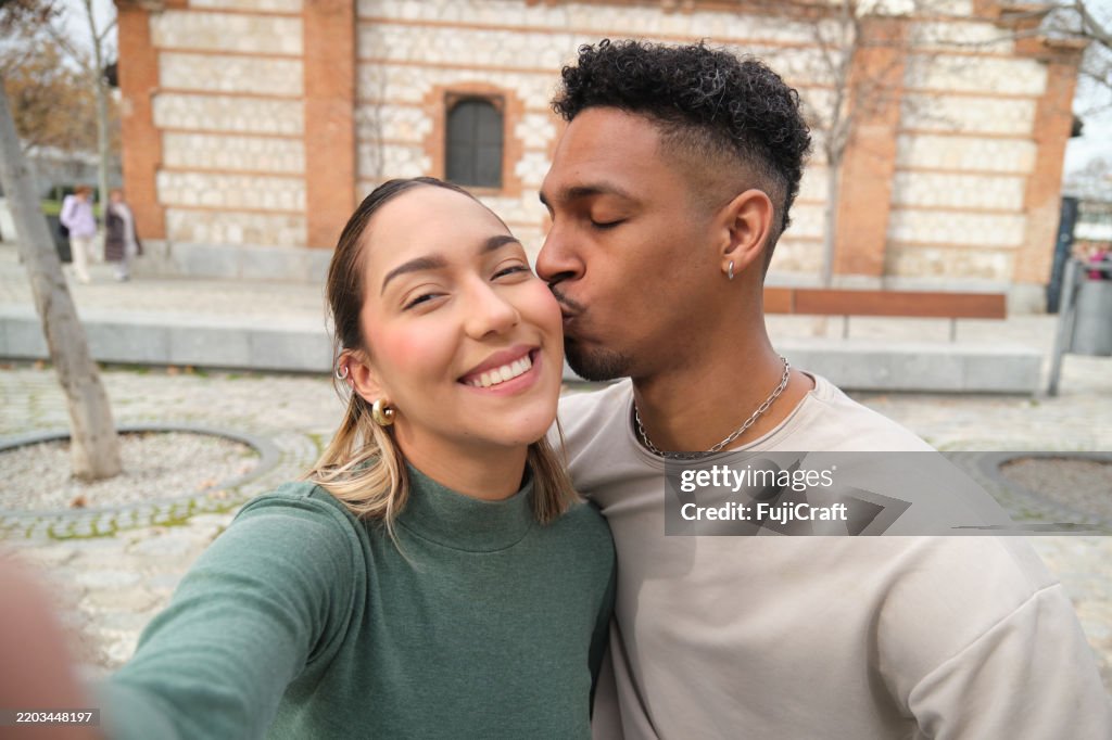 Young couple taking a selfie while kissing in a city park