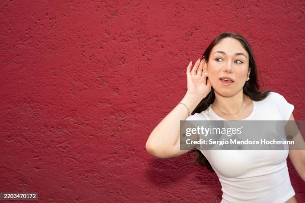 young latino woman putting her hand to her ear and listening intently - handen over de oren stockfoto's en -beelden