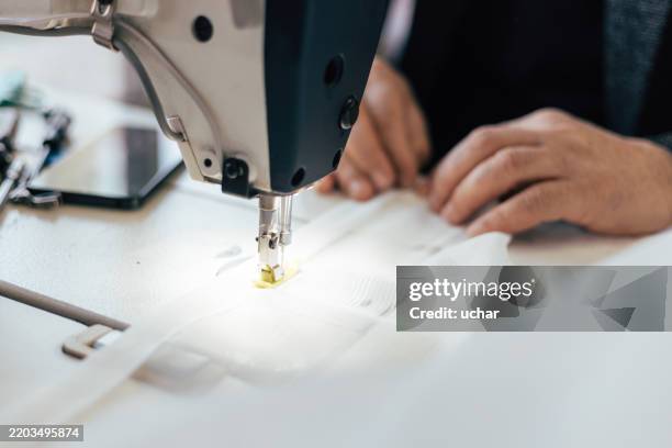 close-up of a tailor using an industrial sewing machine, stitching white fabric and showcasing the precision of garment creation - seam stock pictures, royalty-free photos & images